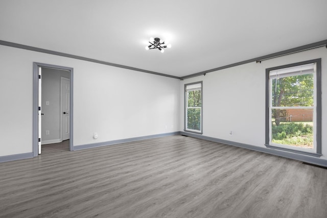 unfurnished room with wood finished floors, visible vents, baseboards, and ornamental molding