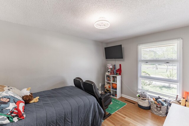  - bedroom with a textured ceiling, wood finished floors, baseboards, and visible vents