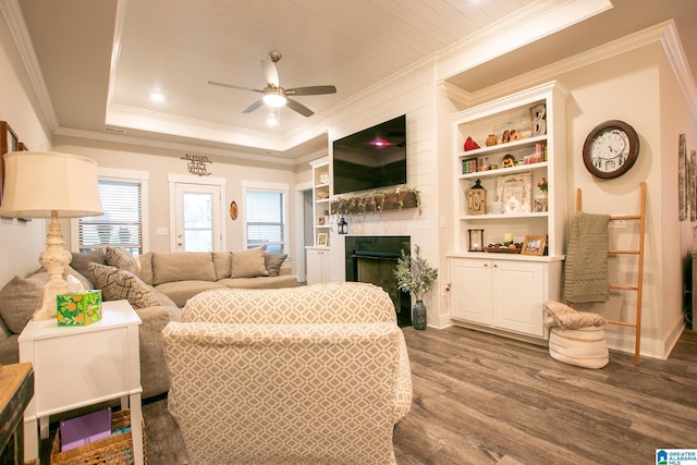  - living area with dark wood-style flooring, a ceiling fan, crown molding, a large fireplace, and a tray ceiling