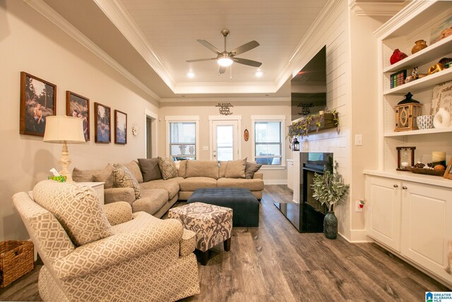  - living room featuring dark wood-style flooring, a ceiling fan, a fireplace, a raised ceiling, and crown molding