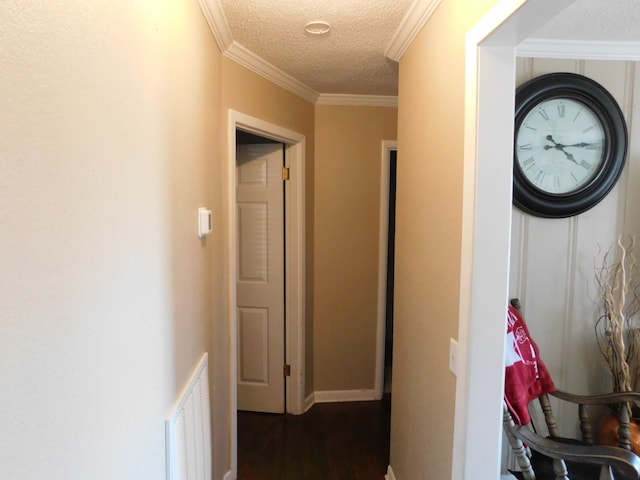 hall with a textured ceiling, visible vents, baseboards, ornamental molding, and dark wood finished floors