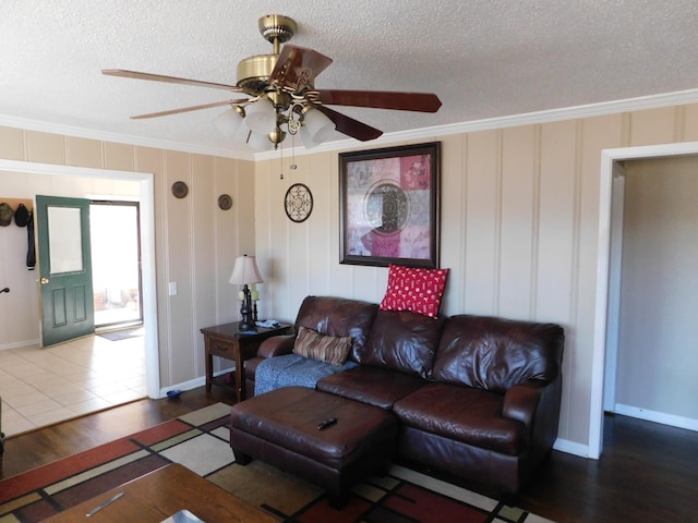 living room featuring baseboards, a textured ceiling, ornamental molding, and wood finished floors