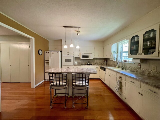  - kitchen with white appliances, a sink, dark wood finished floors, a kitchen island, and a breakfast bar area