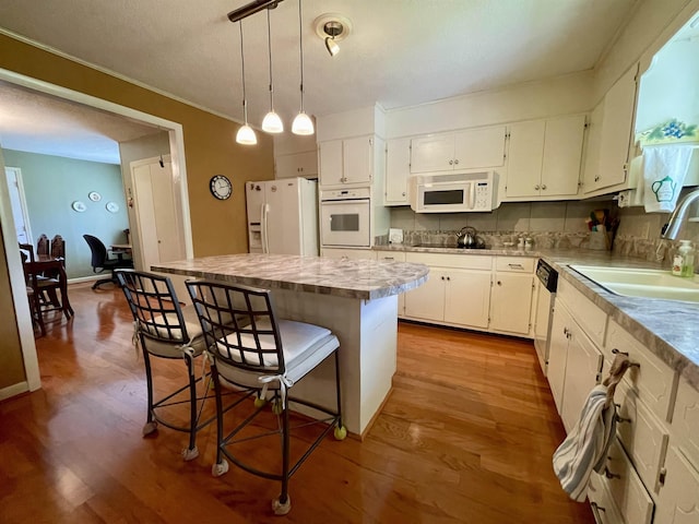  - kitchen featuring white appliances, a sink, white cabinetry, a kitchen island, and a kitchen bar