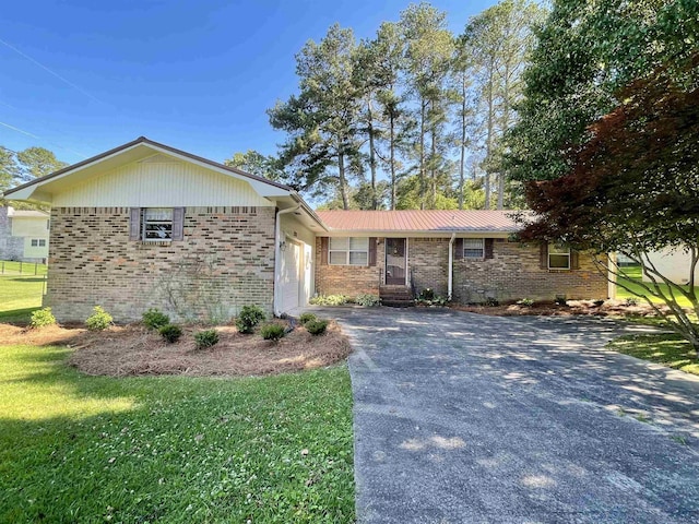  - ranch-style home featuring an attached garage, driveway, brick siding, a front lawn, and metal roof