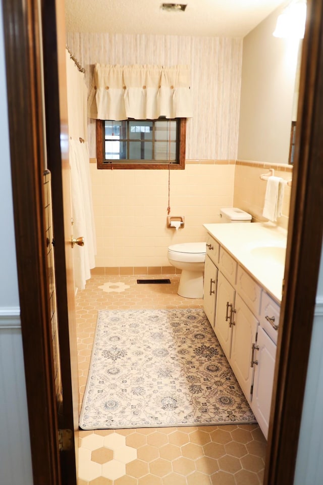 bathroom with tile patterned flooring, vanity, toilet, and tile walls