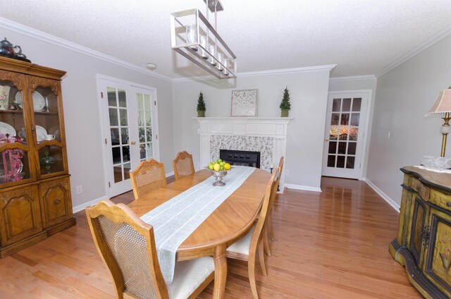 dining area featuring french doors, light wood-type flooring, a textured ceiling, crown molding, and a tiled fireplace