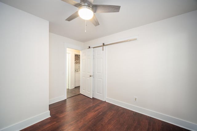 unfurnished bedroom featuring dark hardwood / wood-style flooring, a barn door, ceiling fan, and washer / dryer