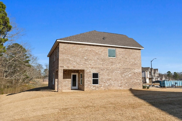 back of property with brick siding, a lawn, and roof with shingles