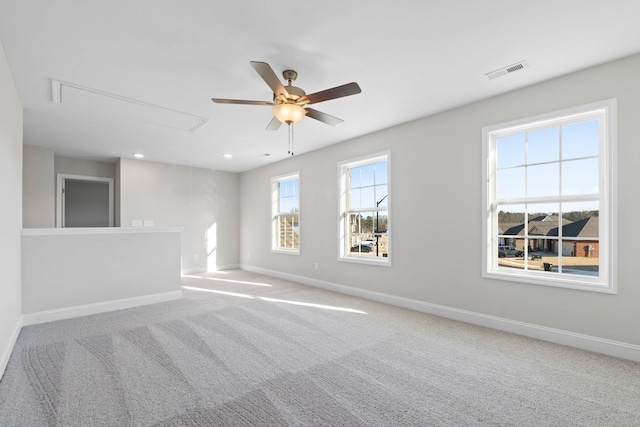 carpeted empty room with attic access, visible vents, baseboards, and a ceiling fan