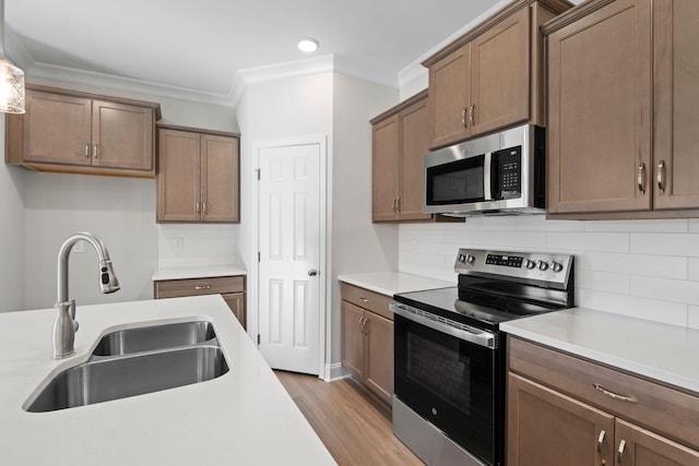 kitchen with wood finished floors, a sink, light countertops, ornamental molding, and appliances with stainless steel finishes