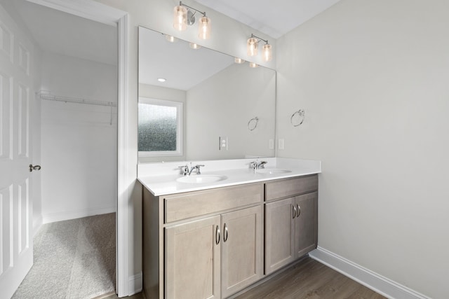 bathroom featuring a walk in closet, a sink, baseboards, and double vanity