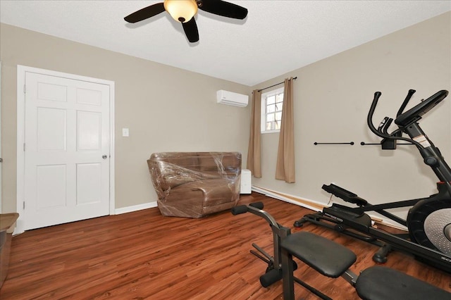 workout area featuring a textured ceiling, a wall unit AC, wood finished floors, a ceiling fan, and baseboards