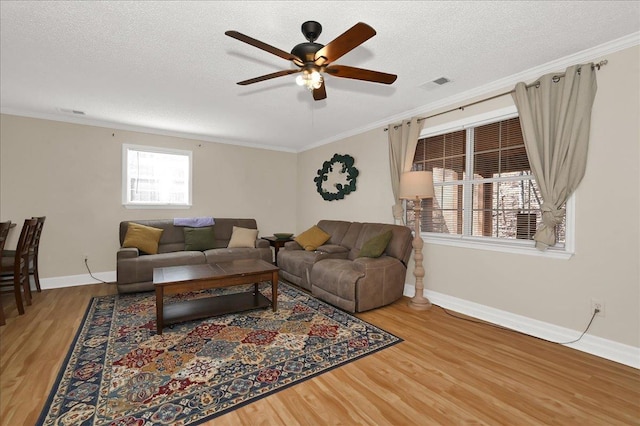 living area with a textured ceiling, visible vents, wood finished floors, and ornamental molding