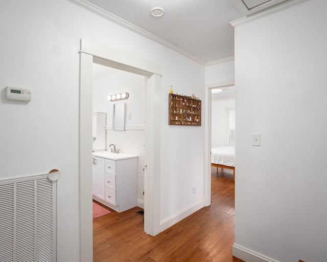 corridor with ornamental molding, light wood-style flooring, visible vents, and baseboards