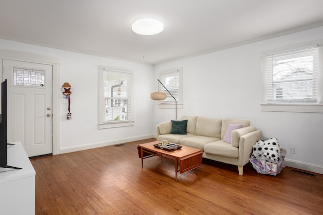 living room featuring a wealth of natural light, visible vents, wood finished floors, and ornamental molding