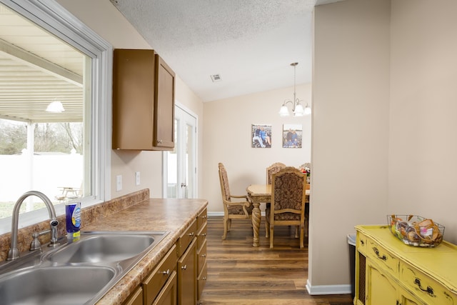 kitchen featuring dark wood-type flooring, sink, pendant lighting, a chandelier, and lofted ceiling