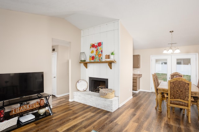 dining area featuring vaulted ceiling, an inviting chandelier, dark wood-type flooring, and a brick fireplace