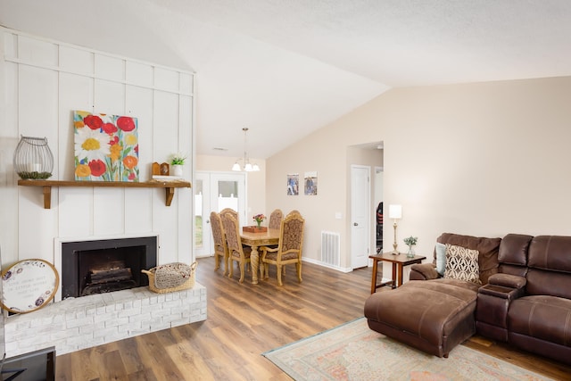 living room featuring a brick fireplace, a notable chandelier, vaulted ceiling, and hardwood / wood-style flooring