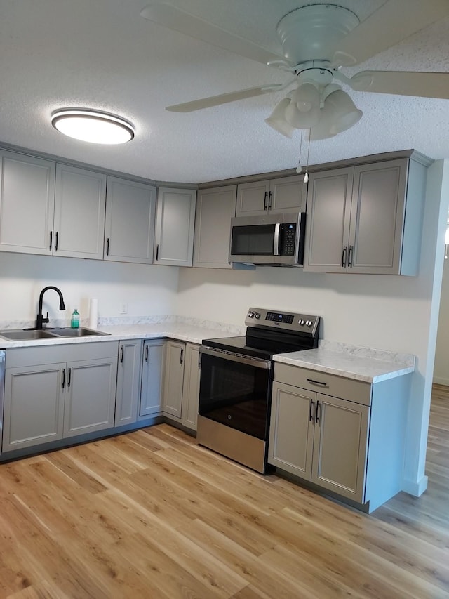 kitchen with gray cabinetry, ceiling fan, sink, stainless steel appliances, and light wood-type flooring