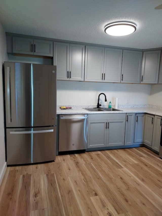 kitchen featuring sink, stainless steel appliances, light hardwood / wood-style floors, a textured ceiling, and gray cabinets