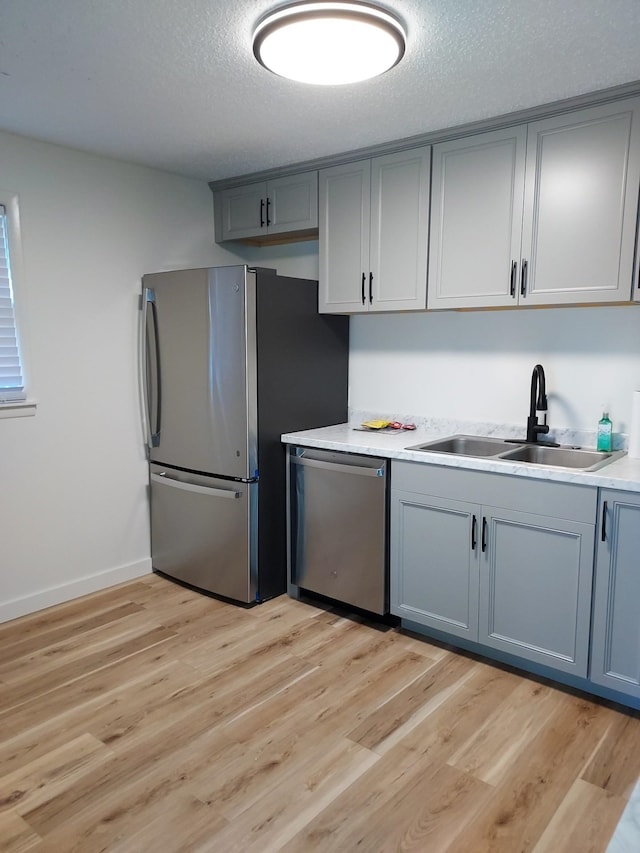 kitchen with gray cabinetry, sink, a textured ceiling, light hardwood / wood-style floors, and stainless steel appliances