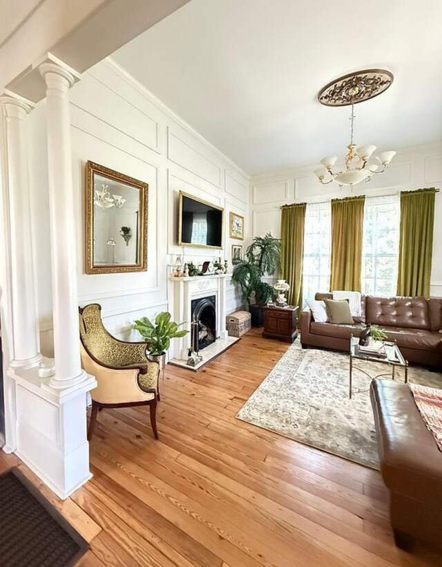  - living area with ornate columns, a decorative wall, a chandelier, light wood finished floors, and a fireplace