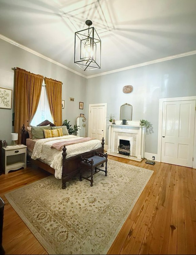  - bedroom with ornamental molding, wood finished floors, a chandelier, and a tiled fireplace