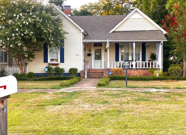 - view of front of property with covered porch, a front yard, roof with shingles, and a chimney