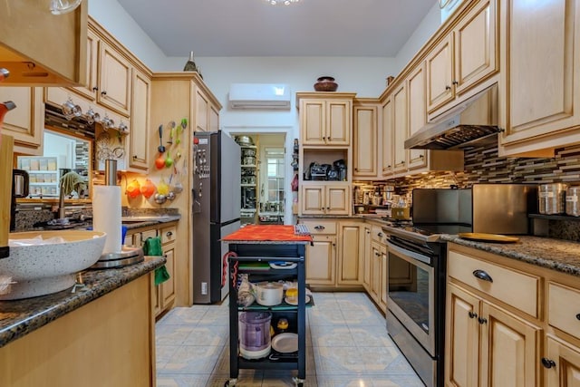 kitchen with light brown cabinets, stainless steel appliances, an AC wall unit, and dark stone countertops