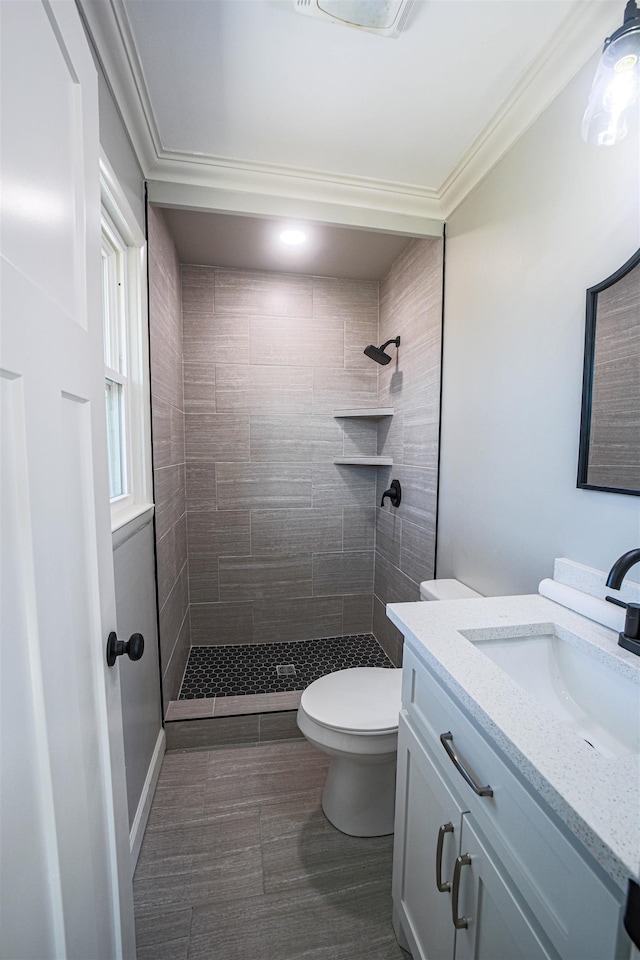 bathroom with crown molding, vanity, toilet, and a tile shower