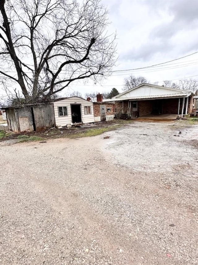 single story home featuring driveway, a carport, and an outbuilding