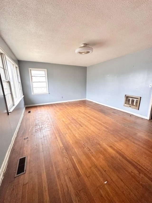 spare room featuring visible vents, a textured ceiling, baseboards, and hardwood / wood-style flooring