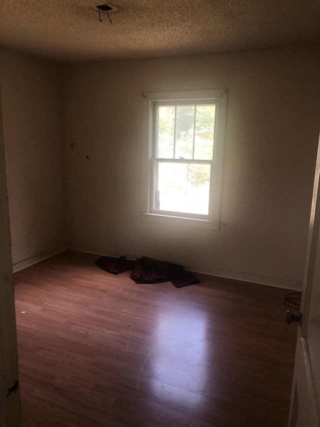  - empty room with wood finished floors, a textured ceiling, and baseboards