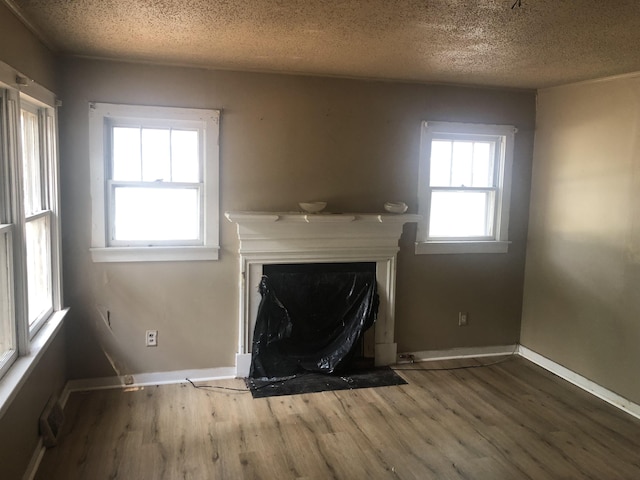  - unfurnished living room with a fireplace with flush hearth, wood finished floors, a textured ceiling, and baseboards