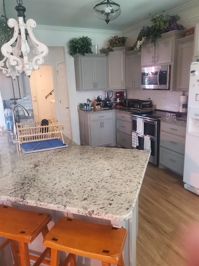 kitchen with backsplash, gray cabinetry, a breakfast bar, stainless steel appliances, and hanging light fixtures