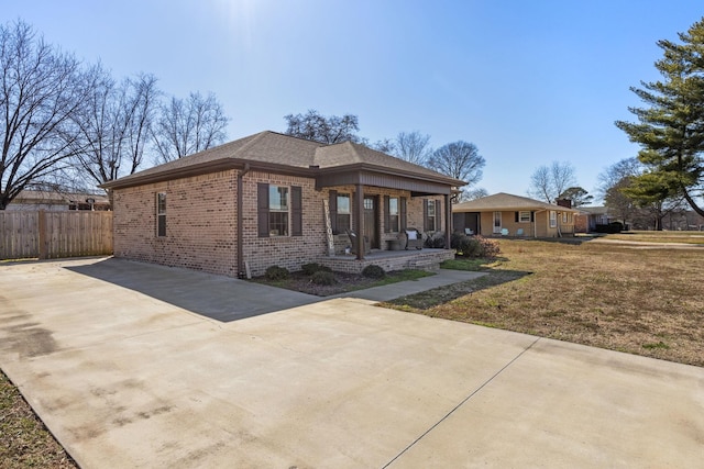 view of front of home with driveway, brick siding, fence, a porch, and a front yard