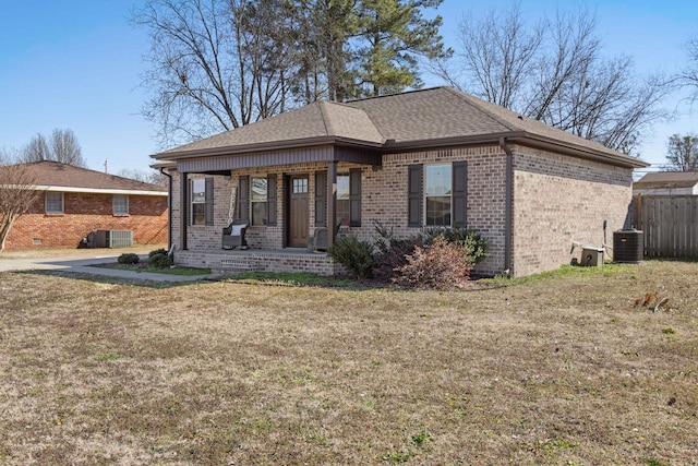 view of front facade with cooling unit, covered porch, brick siding, fence, and a front yard