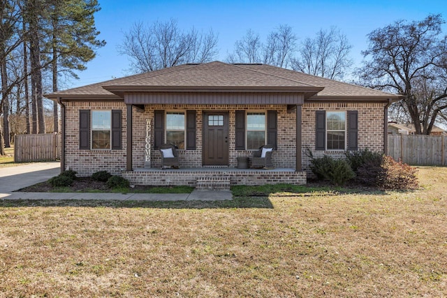 view of front facade with brick siding, a shingled roof, covered porch, fence, and a front lawn