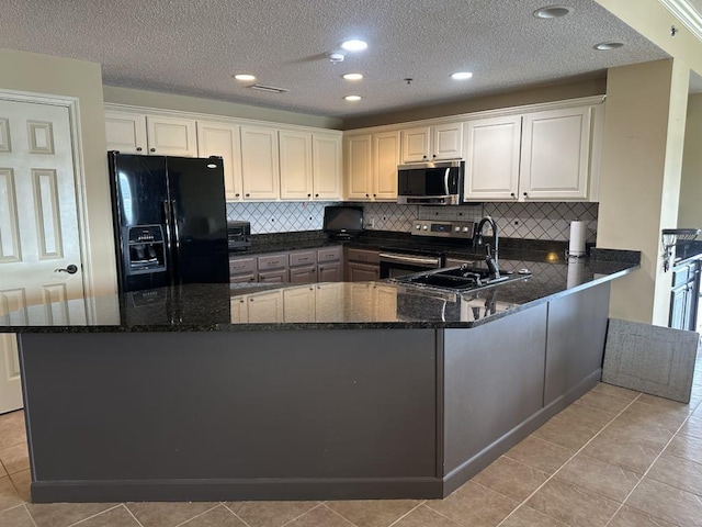  - kitchen featuring stainless steel appliances, a sink, dark stone countertops, backsplash, and a textured ceiling