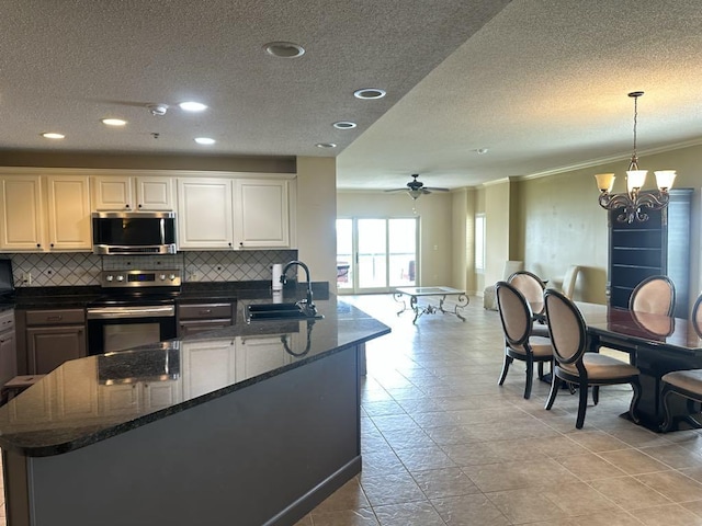  - kitchen with appliances with stainless steel finishes, a sink, a textured ceiling, tasteful backsplash, and a chandelier