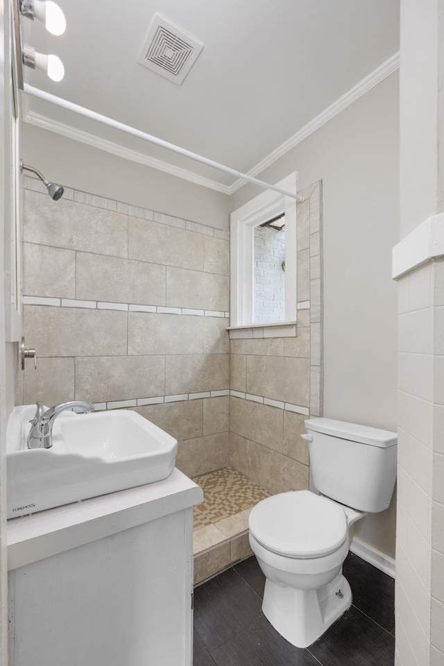 bathroom featuring a tile shower, vanity, toilet, and ornamental molding