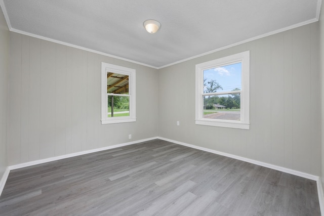 empty room with a textured ceiling, hardwood / wood-style flooring, a wealth of natural light, and ornamental molding