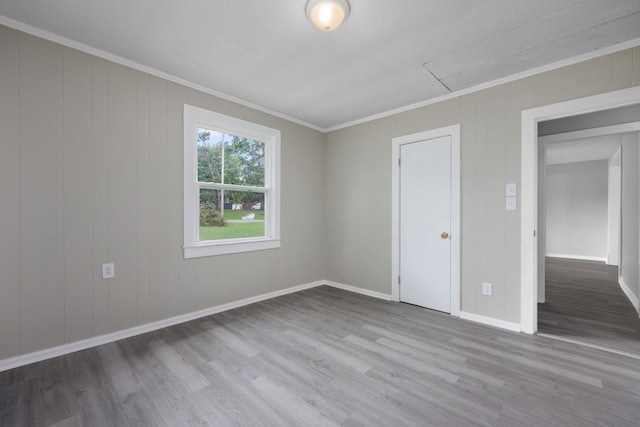 empty room featuring a textured ceiling, light hardwood / wood-style flooring, and crown molding