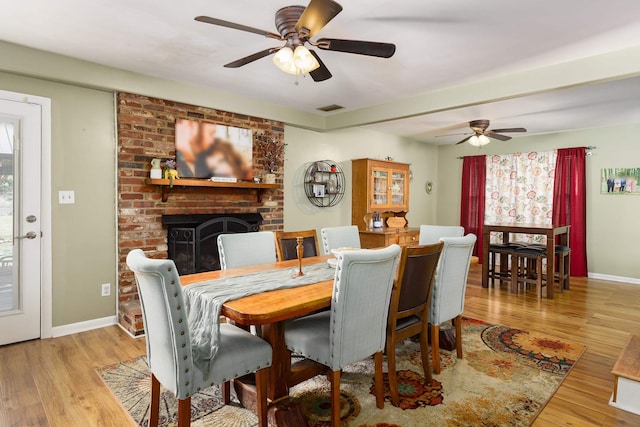  - dining area with visible vents, wood finished floors, ceiling fan, and a brick fireplace