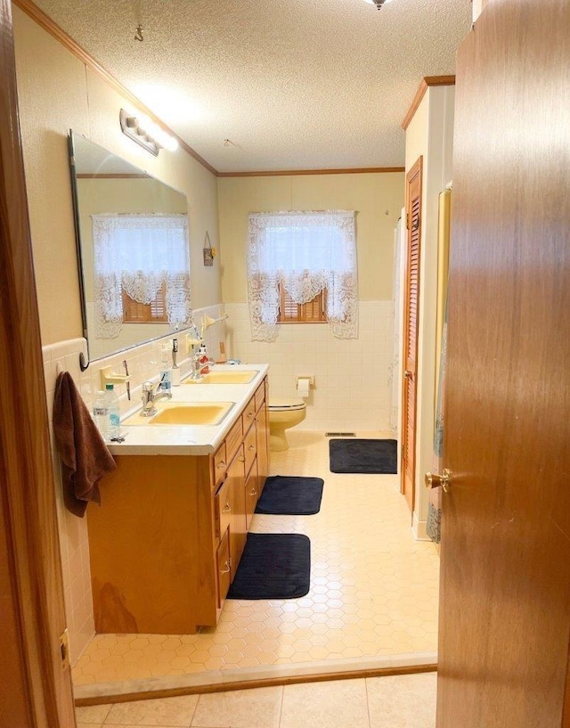 bathroom with a textured ceiling, vanity, crown molding, and tile walls