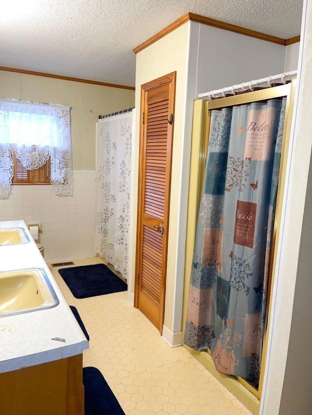 bathroom with a textured ceiling, vanity, ornamental molding, and tile walls