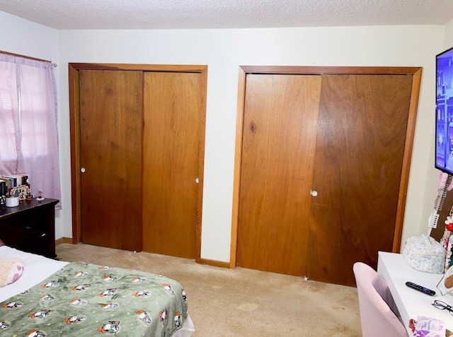 carpeted bedroom with a textured ceiling and multiple closets