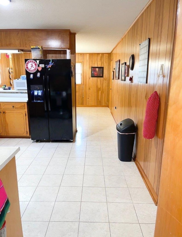 kitchen with black refrigerator with ice dispenser, light tile patterned floors, and wood walls