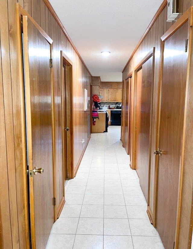 hallway with wood walls, ornamental molding, and light tile patterned floors